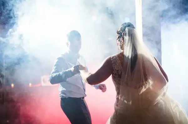 Braut im Hochzeitskleid mit Schleier tanzt mit Bräutigam im Nebellicht.