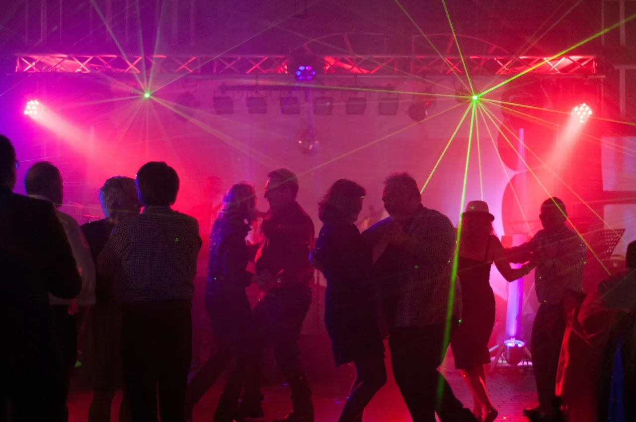 Tanzende Gäste auf Party mit Laserlicht und Nebel, Eventbeleuchtung rot-grün